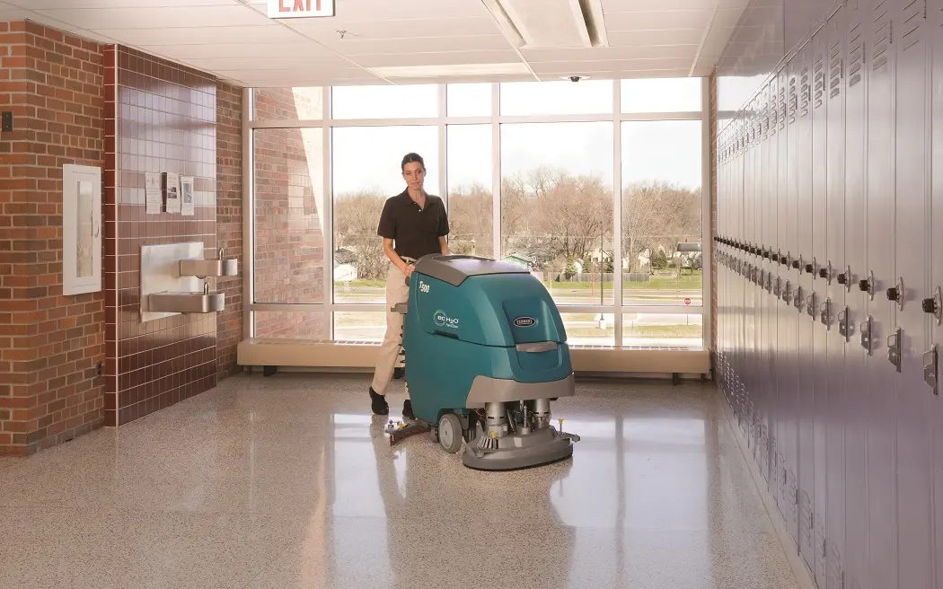 Een vrouw met een schrobmachine die op een Trojan accu werkt